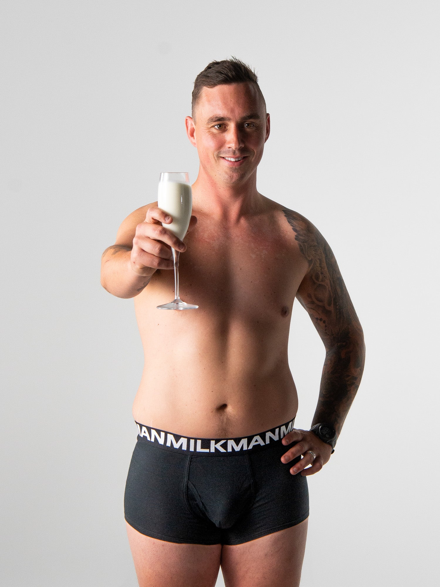 Man wearing black underwear with &#39;Milkman&#39; branding, holding a glass of milk.